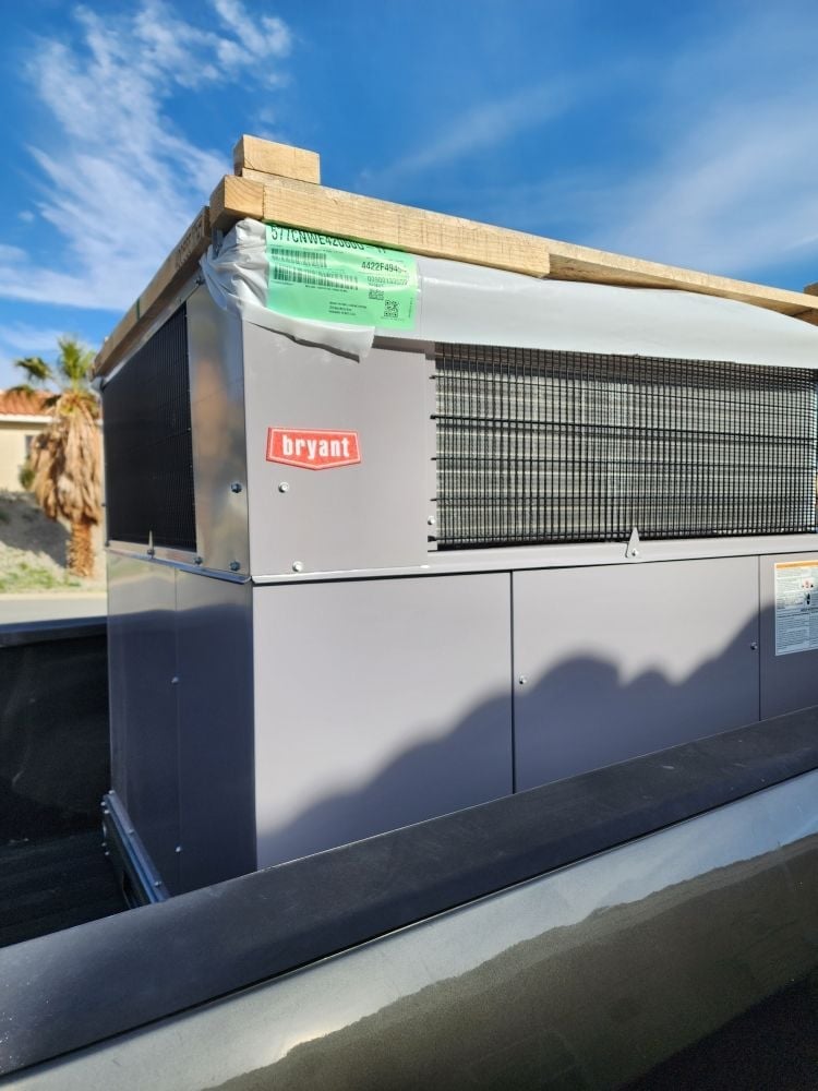 Bryant HVAC unit mounted on rooftop with wooden frame, green energy label, and metal condenser fins visible under blue sky