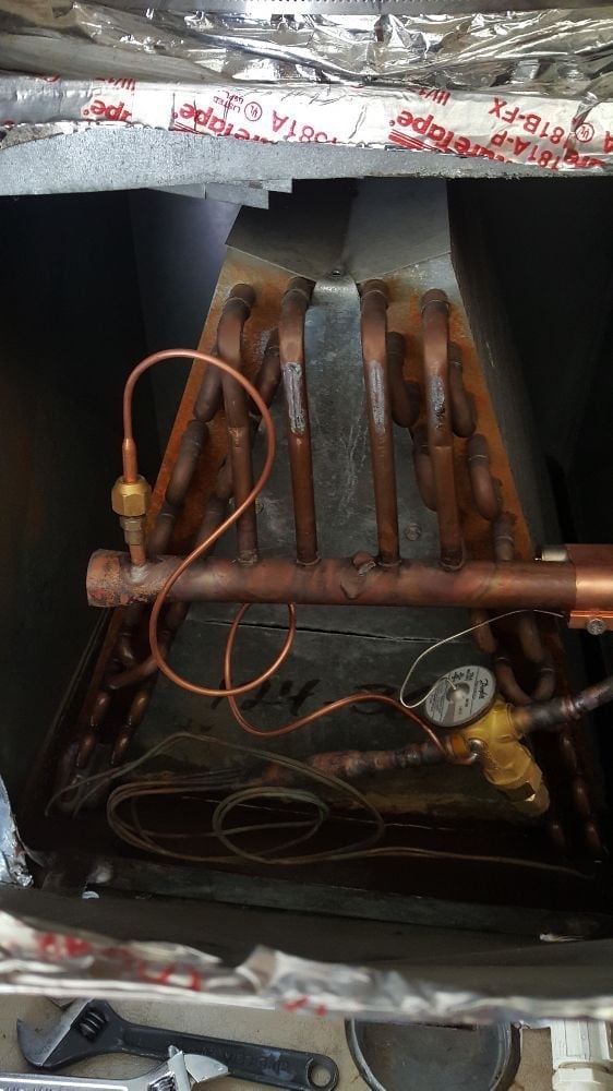 Interior view of HVAC system showing copper pipes, coils, and electrical connections inside dark metal housing