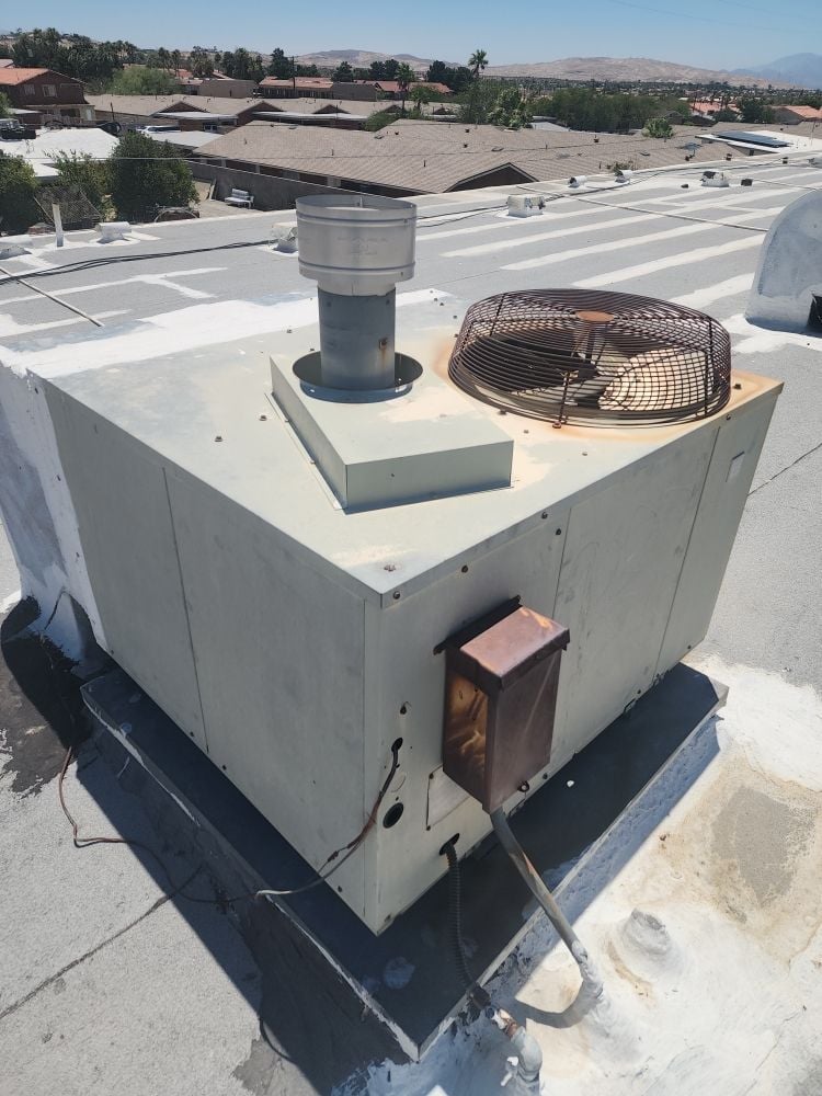 HVAC rooftop unit with metal exhaust vent and fan mounted on white platform against industrial building backdrop
