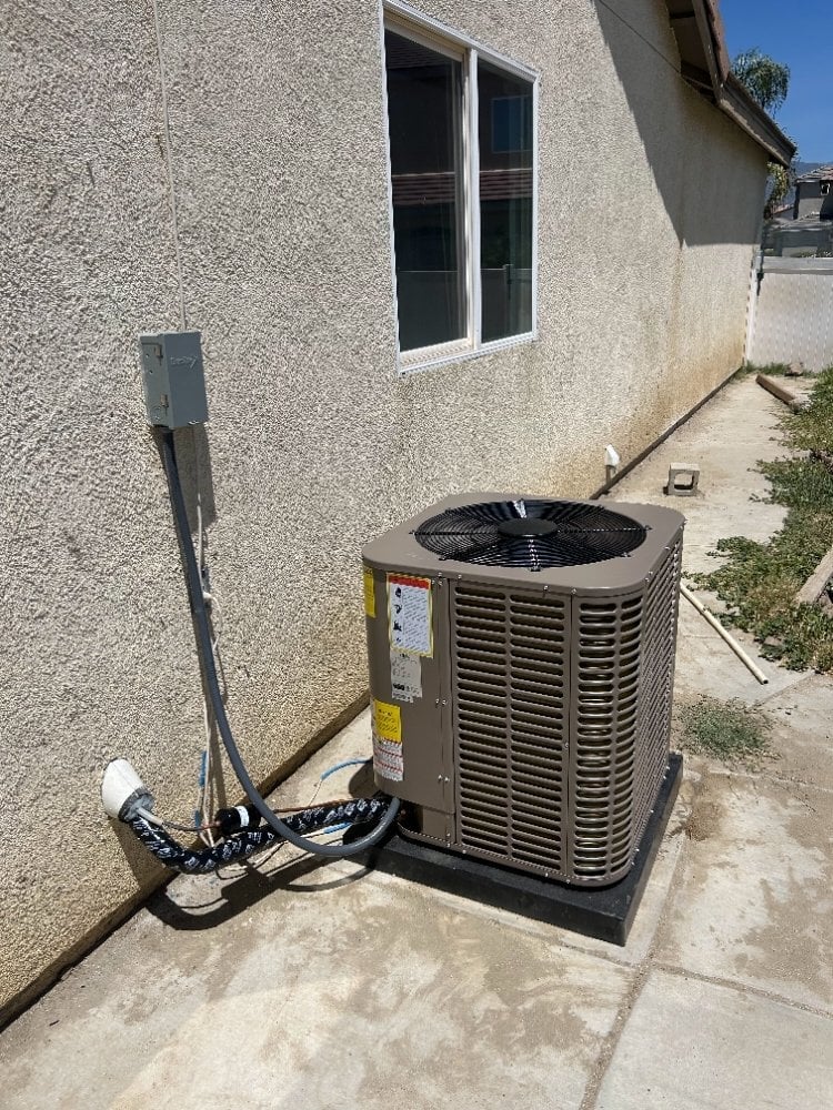Outdoor air conditioning unit installed against a concrete foundation next to a residential building with a window